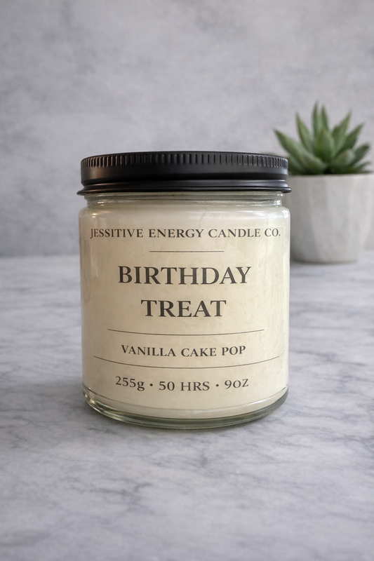 Candle jar labeled 'Birthday Treat Vanilla Cake Pop' on a gray surface with a plant in the background.
